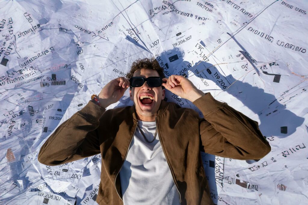 A happy man in sunglasses lying on a pile of documents with a euphoric smile.